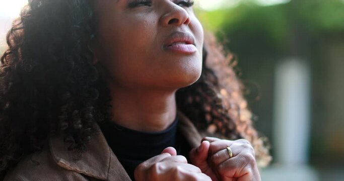 African woman praying to God outside seeking faith and HOPE outside in sunlight