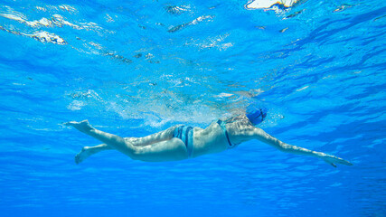 Swimming Girl Athlete unrecognizable training freestyle stroke underwater photography closeup upward view in blue pool water.