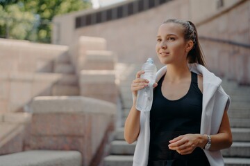 Athlete woman with pony tail feels thirsty after cardio training drinks water from bottle holds...