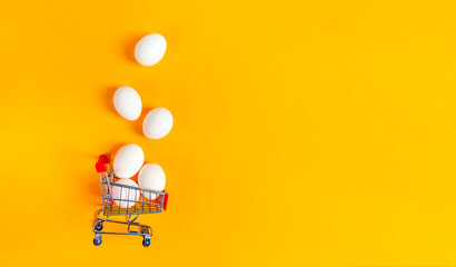 Commercial concept with eggs. Shopping basket and white eggs on yellow background. Banner. Copy space