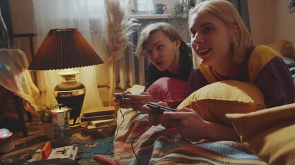 Young Caucasian couple smiling and chatting while lying together on bed at home and playing retro console game