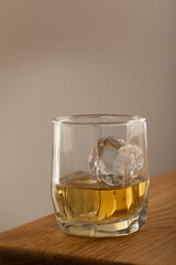 Whiskey or alcoholic beverage, with ie in a square formed designer glass. Sitting on an Oak table, with a backlighted gray surface.