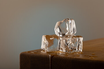 3 blocks of ice melting on a oak table, with a blue shined background on a grey surface. With...