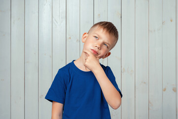 Portrait of dreamy preteen boy in blue t shirt daydreaming about having something, touching chin...