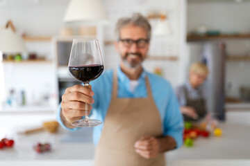 Happy senior couple cooking together and drinking wine in home kitchen