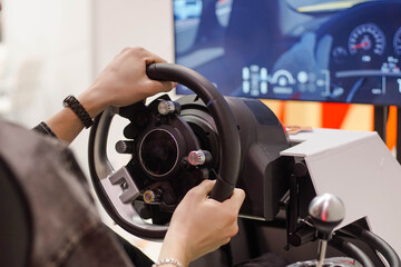 Teen man playing racing simulator game with big screen monitor in theme park.