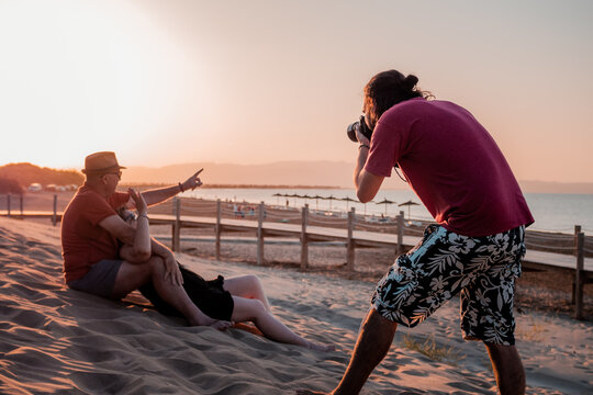 Male photographer taking photos of couple resting on beach