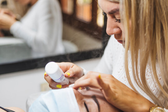 Crop beautician applying eyelashes on face of woman