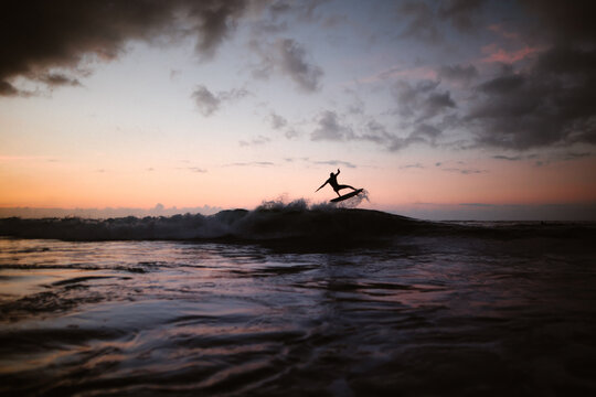 Unrecognizable athlete practicing surfing on ocean wave at sunset