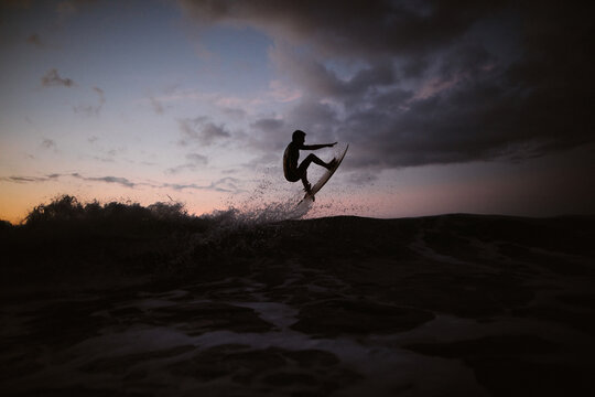 Unrecognizable athlete practicing surfing on ocean wave at sunset