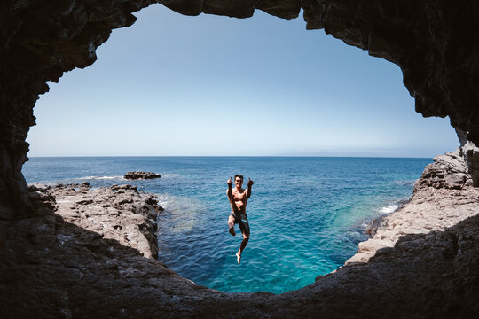 Smiling man showing fuck gesture while jumping over sea