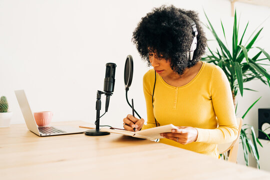 Young black lady writing notebook while recording podcast in studio