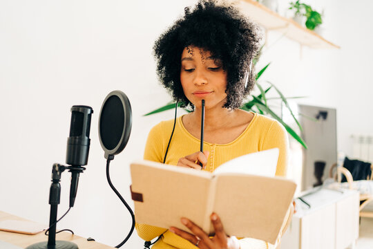 Young black lady reading notebook while recording podcast in studio