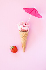 Strawberry ice cream cone with decorative umbrella on the pink background, top view