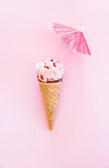 Strawberry ice cream cone with decorative umbrella on the pink background, top view