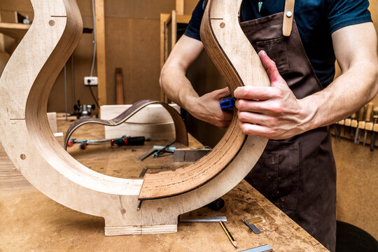 Anonymous luthier building guitar at table in workshop