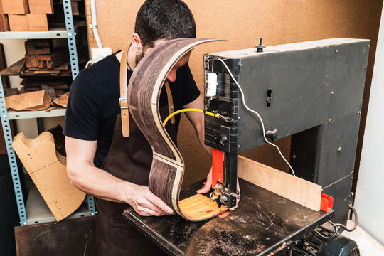 Anonymous luthier cutting guitar body on bandsaw in workroom
