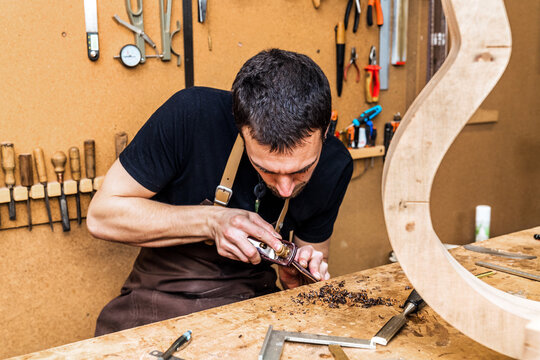 Focused artisan working with wood while building guitar