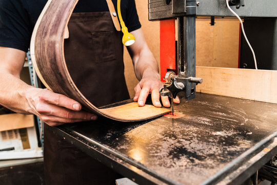 Anonymous luthier cutting guitar body on bandsaw in workroom