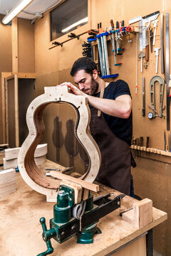 Craftsman building guitar in workshop with assorted instruments