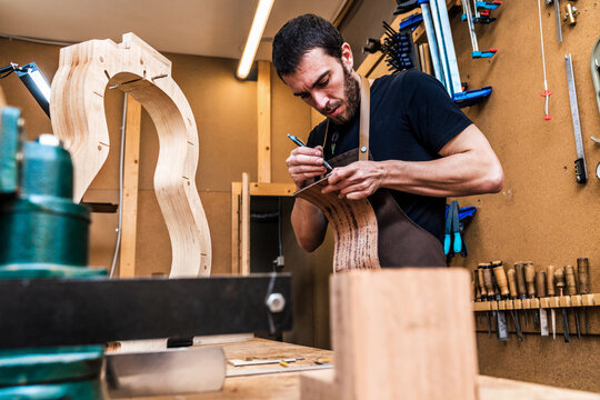 Luthier marking wooden piece while building guitar in workshop