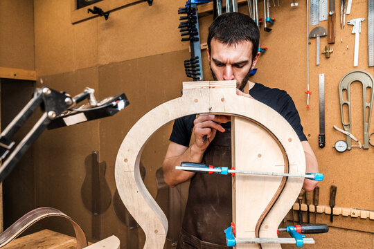 Craftsman building guitar in workshop with assorted instruments