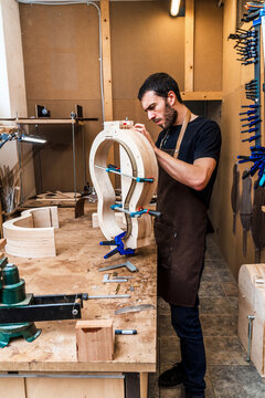 Craftsman building guitar in workshop with assorted instruments