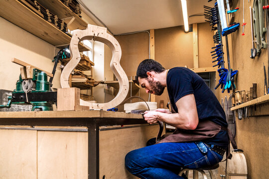 Focused artisan working with wood while building guitar