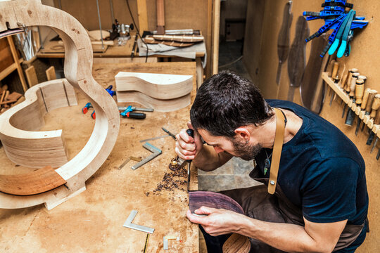 Luthier with rasp building guitar at table in workroom