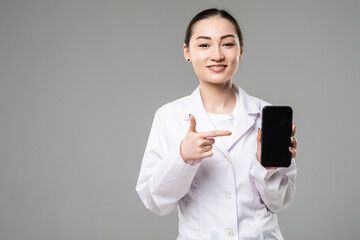 Asian female doctor smiling and showing a blank smart phone screen isolated on a white background