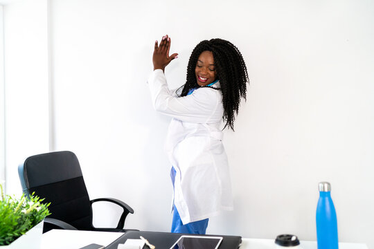 Black female doctor in medical uniform dancing in clinic