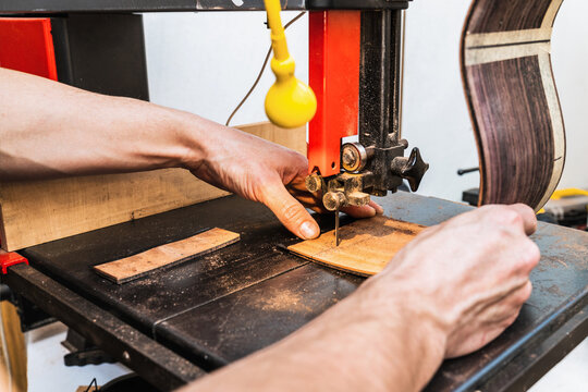 Anonymous luthier cutting guitar body on bandsaw in workroom