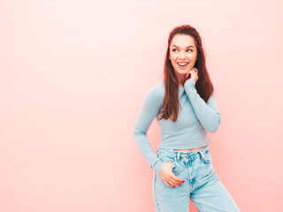 Obraz premium Young beautiful smiling female in trendy summer hipster clothes. Sexy carefree woman posing near light blue wall in studio. Positive model having fun indoors. Cheerful and happy