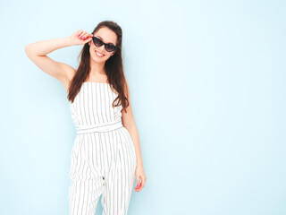 Naklejka premium Young beautiful smiling female in trendy summer hipster clothes. Sexy carefree woman posing near light blue wall in studio. Positive model having fun indoors. Cheerful and happy