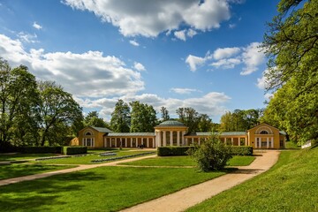 Marianske Lazne, Czech Republic - June 1 2021: The Ferdinand spring pavilion, a yellow building, standing in a park with green lawn and trees. Sunny day with blue sky and clouds.