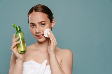 Ginger woman wearing towel cleaning her face with face lotion