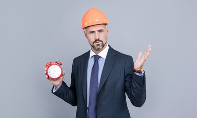 architect man in businesslike suit and hardhat holding alarm clock, time management