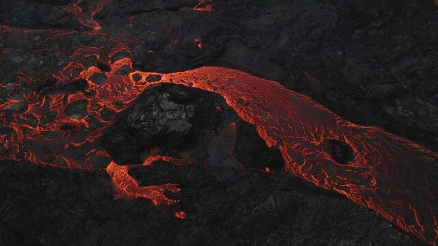 Red lava river flowing slowly through black solidified rocks. Aerial static view