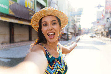 Young brunette woman using a mobile phone takes a selfie with attractive smile. Happy Hispanic girl...