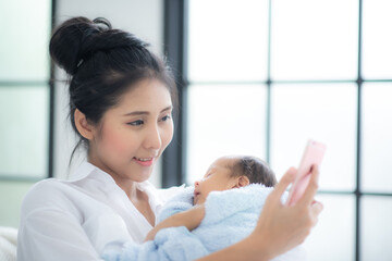 A asian mother is holding newborn baby. Mom of a nursing baby. Mother taking a photo of her infant, family at home. Portrait of a happy mother and chil, family concept.