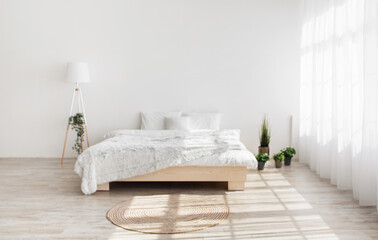 Plants in pots in interior of modern bedroom. Double bed with pillows and blanket, plants, lamp, carpet on floor