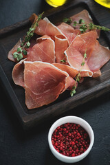 Rustic wooden serving tray with jamon or dry-cured ham slices, vertical shot on a black stone surface