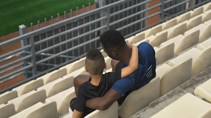 Diverse father and son hugging and watching match on stadium