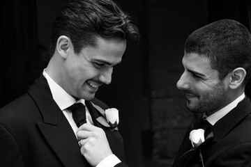 Gay couple laughing outside of church with one groom adjusting his husband's tie