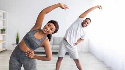 Millennial black couple doing lateral flexion exercise, working out together at home during...