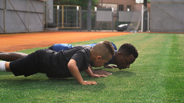 Diverse trainer and boy doing push ups on field - Powered by Adobe