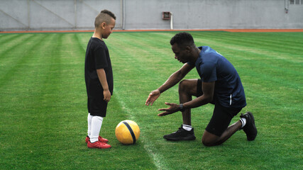 Black father teaching son to handle football ball