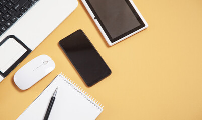 White laptop computer, smartphone, notepad, pen, tablet and mouse on yellow background.