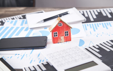 House model with calculator, graphs, pen, notepad, smartphone.