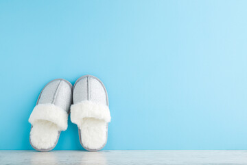 Beautiful soft warm female gray slippers with white fur on wooden floor at light blue wall...